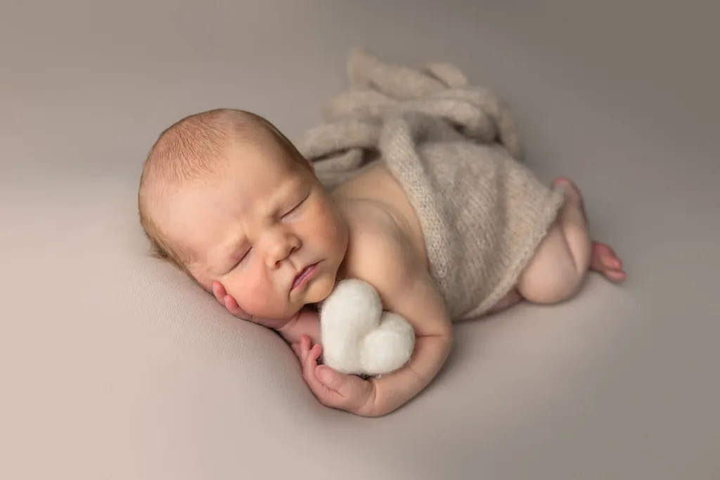 En liten nyfödd baby som håller ett hjärta.