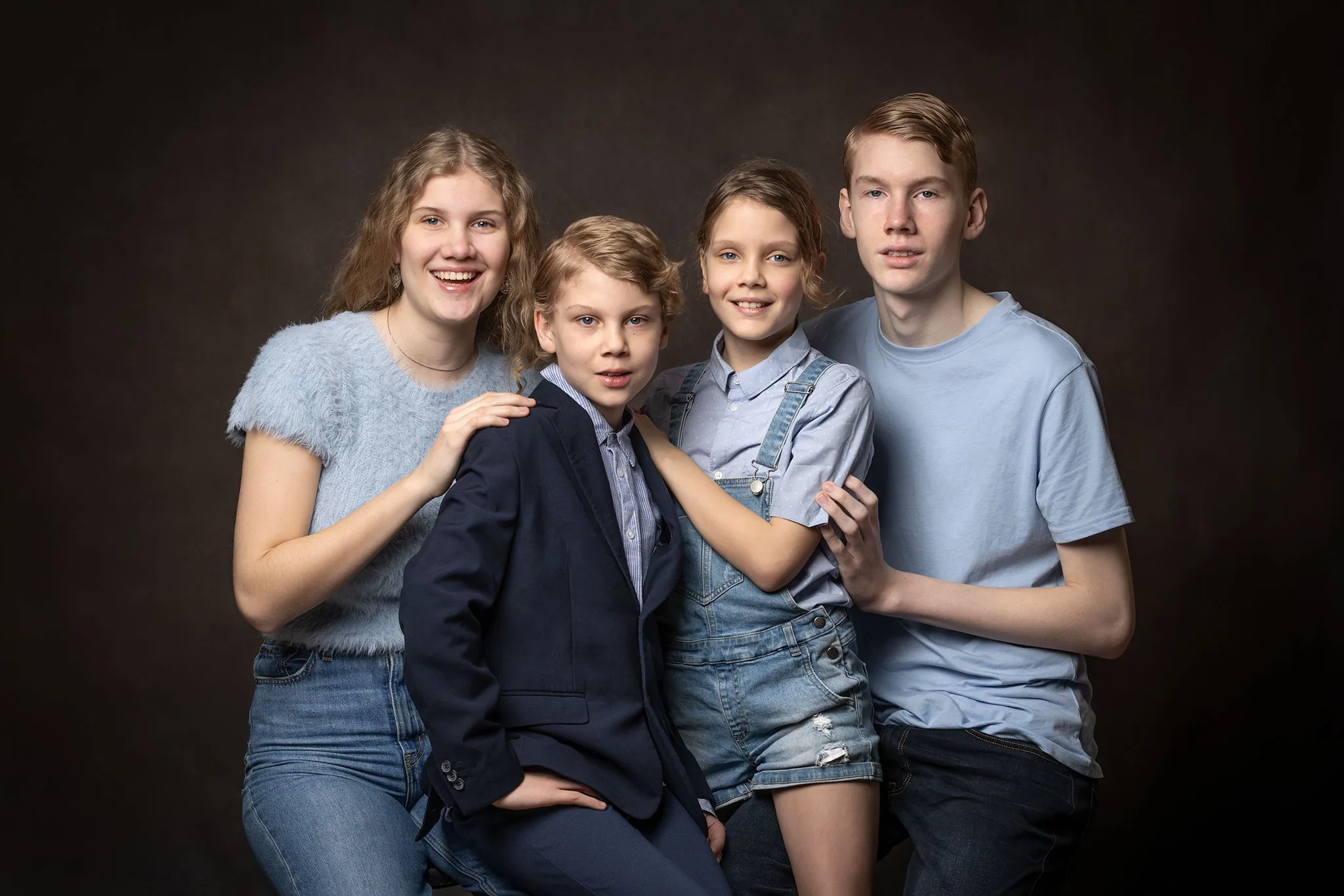 4 syskon i olika åldrar som är klädda i blåa kläder till brun bakgrund.