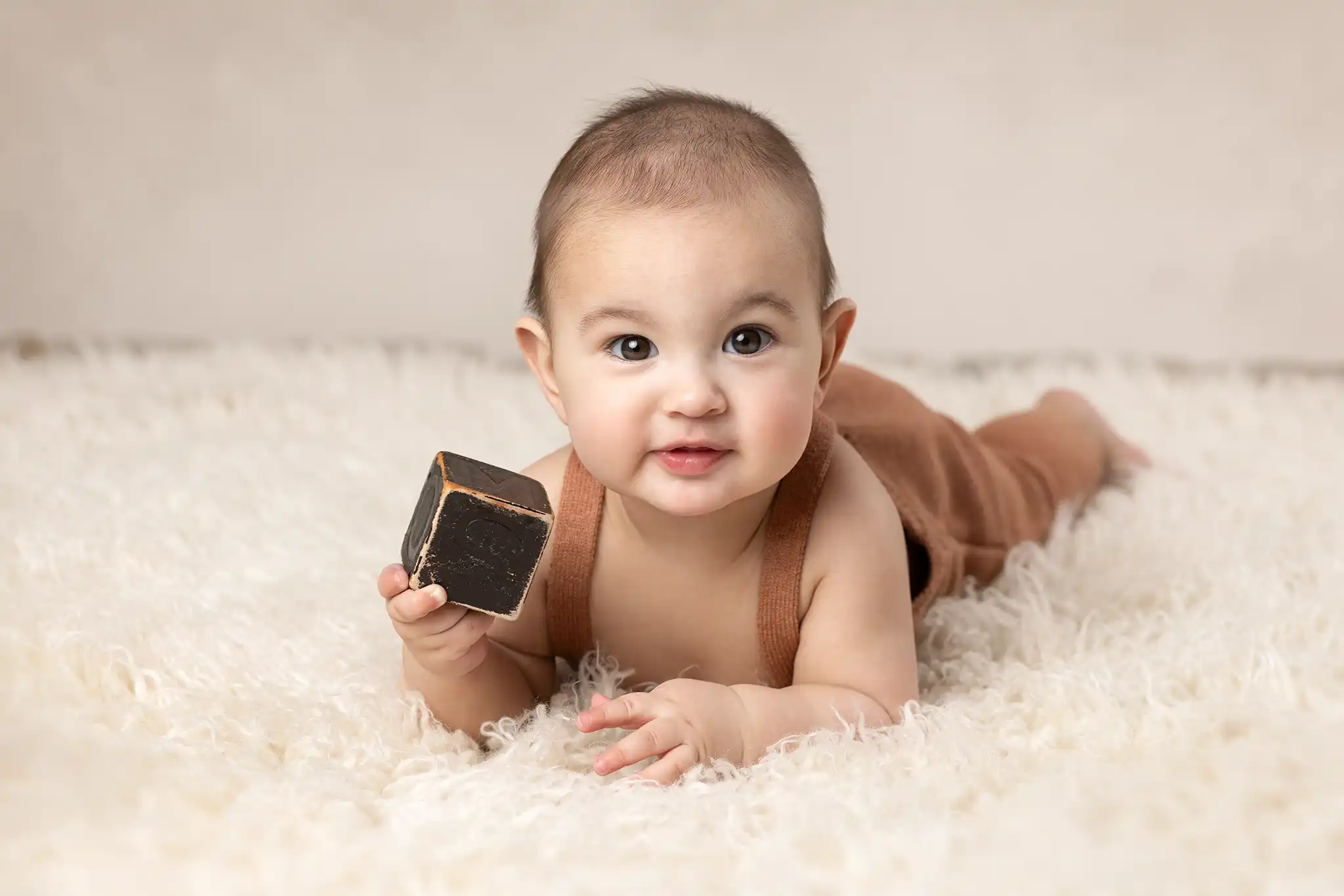 6 månaders baby ligger på fällen med en kloss och ler.