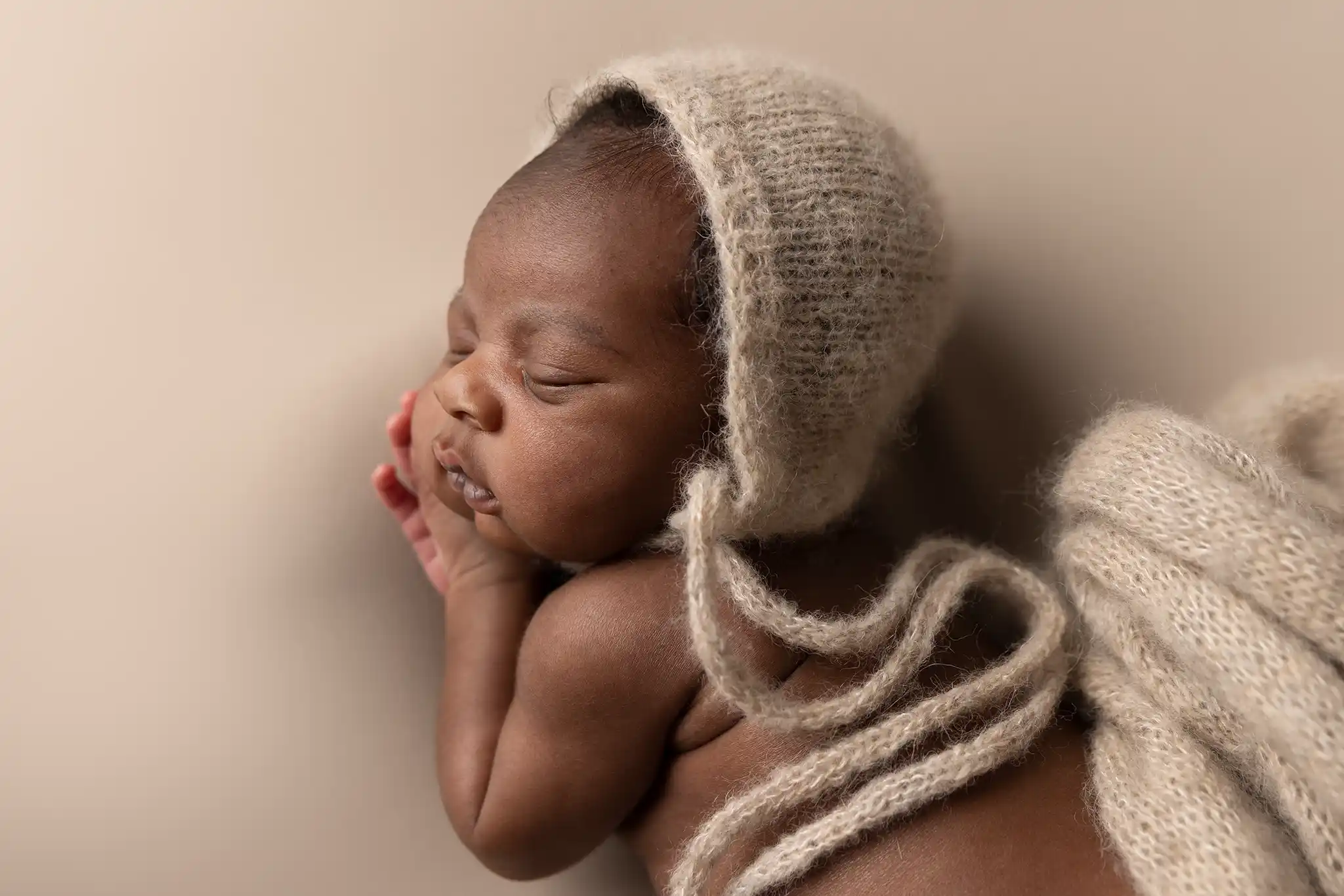 Newbornfotografering i mjuka texturer Nyfödd baby poserar sovandes inlindad i stickat material.