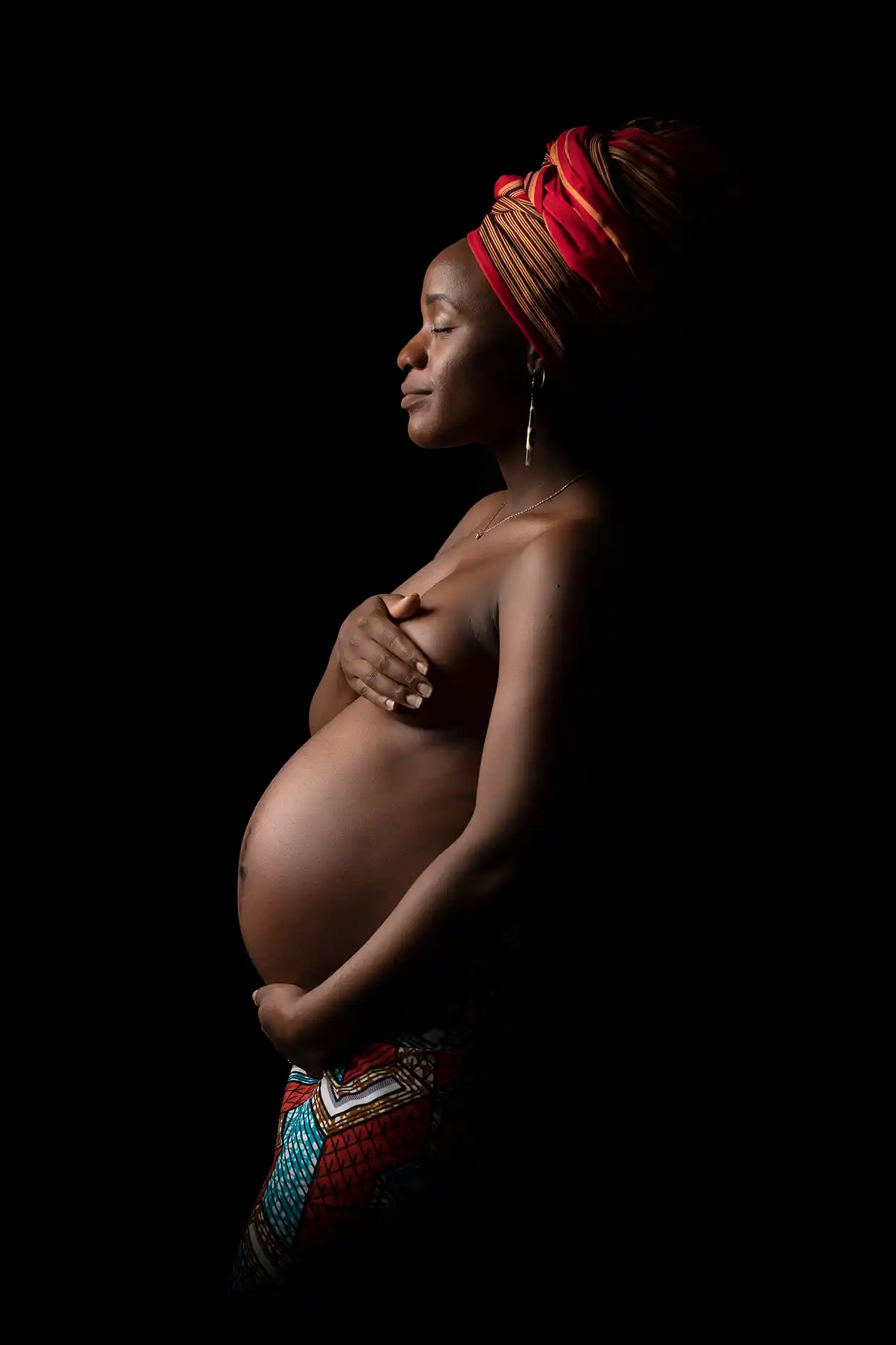 Gravid kvinna med färgglad turban i profil mot svart bakgrund.