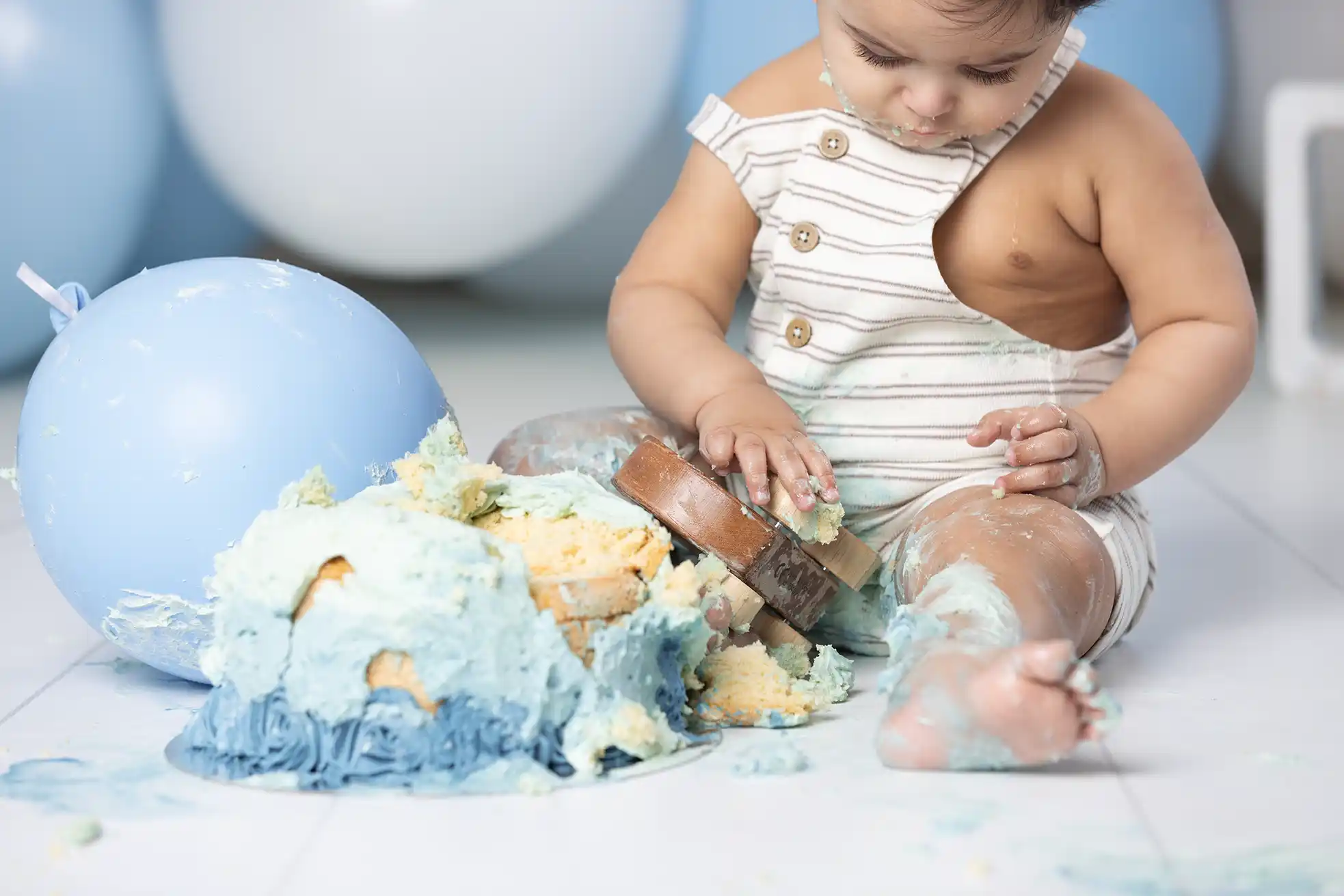 Kladdigt och kul med smash the cake Liten pojke smetar blå tårta på benet under ettårsfotografering.