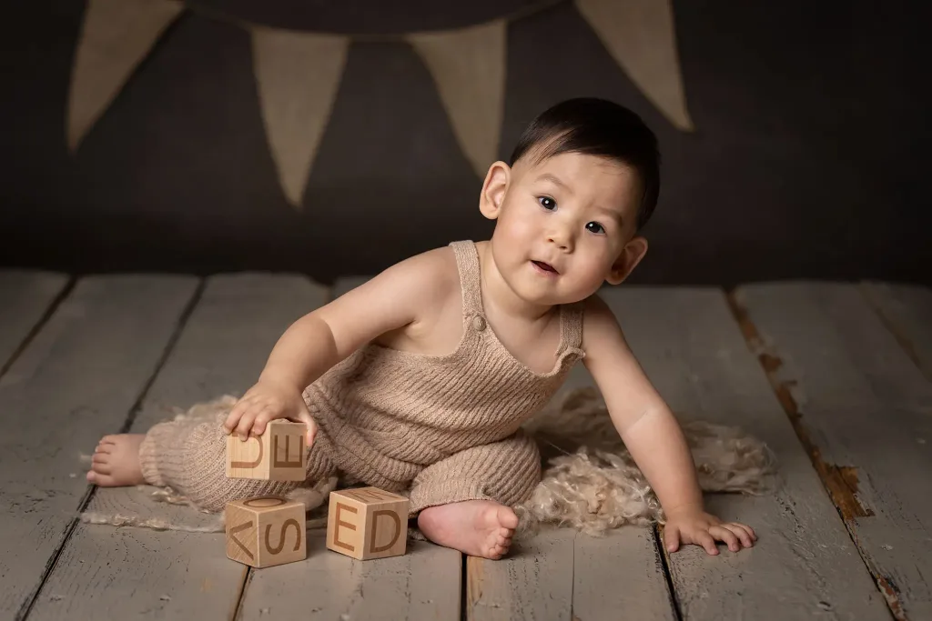Nyfiken baby tittar in i kameran och håller i träklossar på vintagegolv.