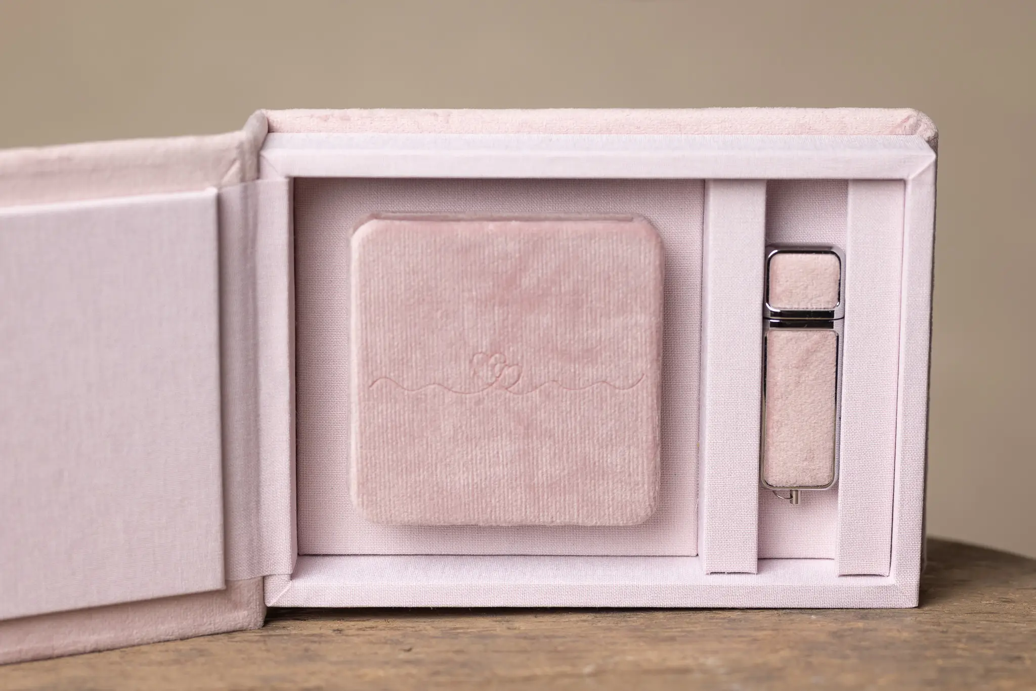 Närbild av rosa sammetsbox med minialbum och USB-minne på träunderlag.