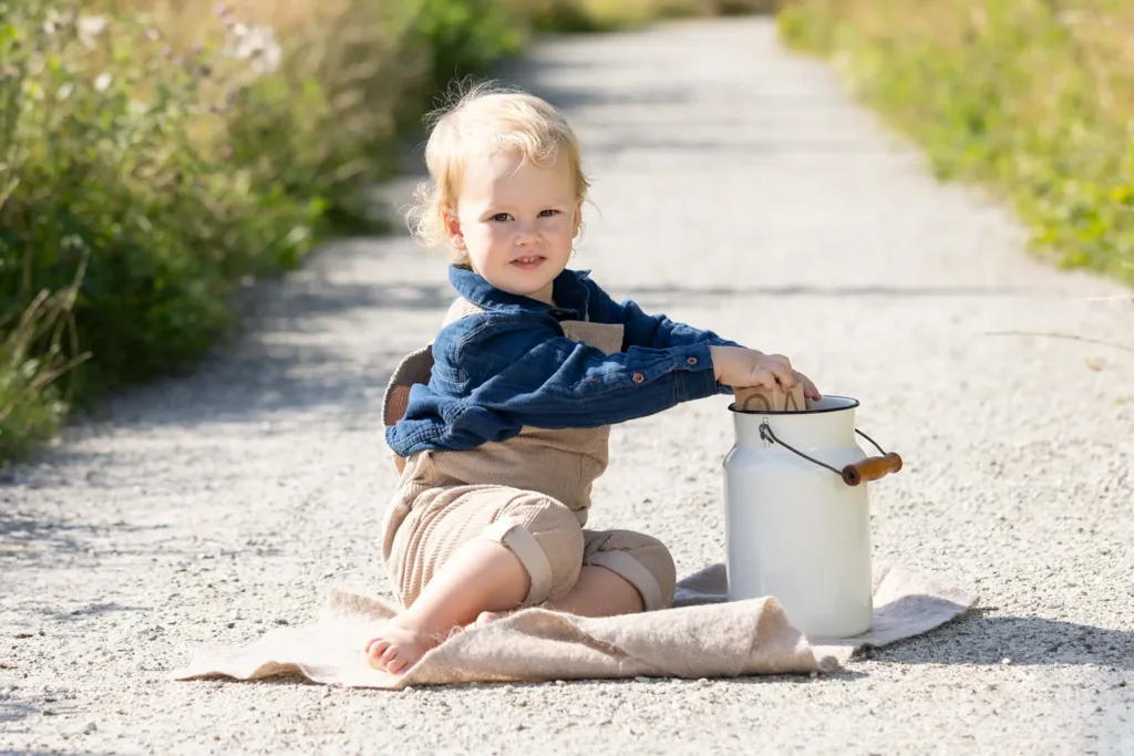 En liten pojke sitter och leker med en mjölkkanna