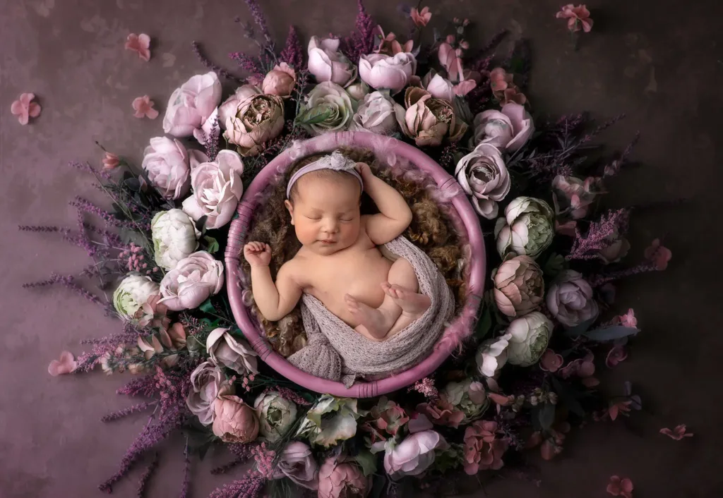 Kreativ nyföddfotografering i Lund med baby inramad av lila och rosa blommor, konstnärligt porträtt av nyfödd.