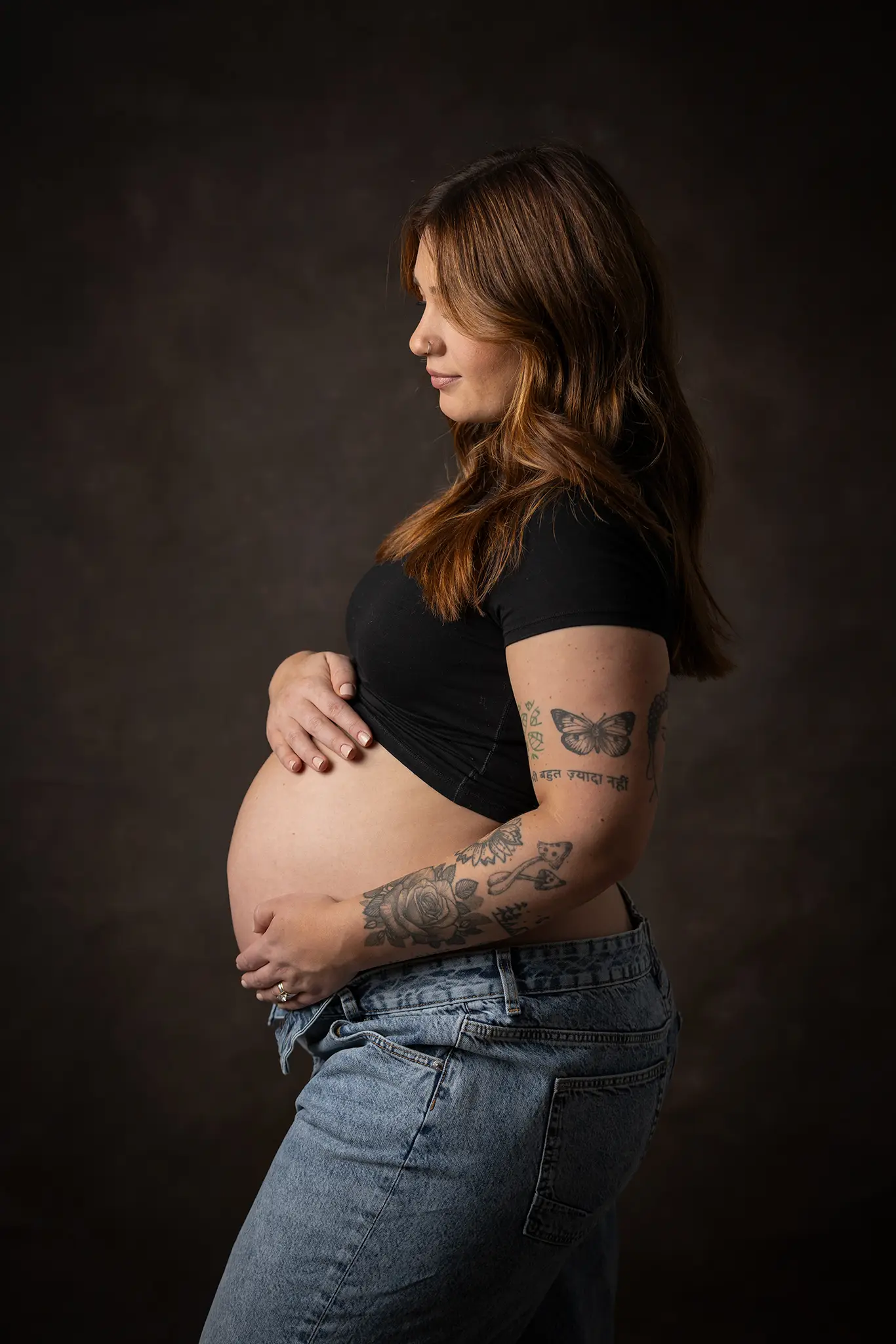 Porträtt av gravid kvinna med tatueringar i studio med mörk bakgrund.