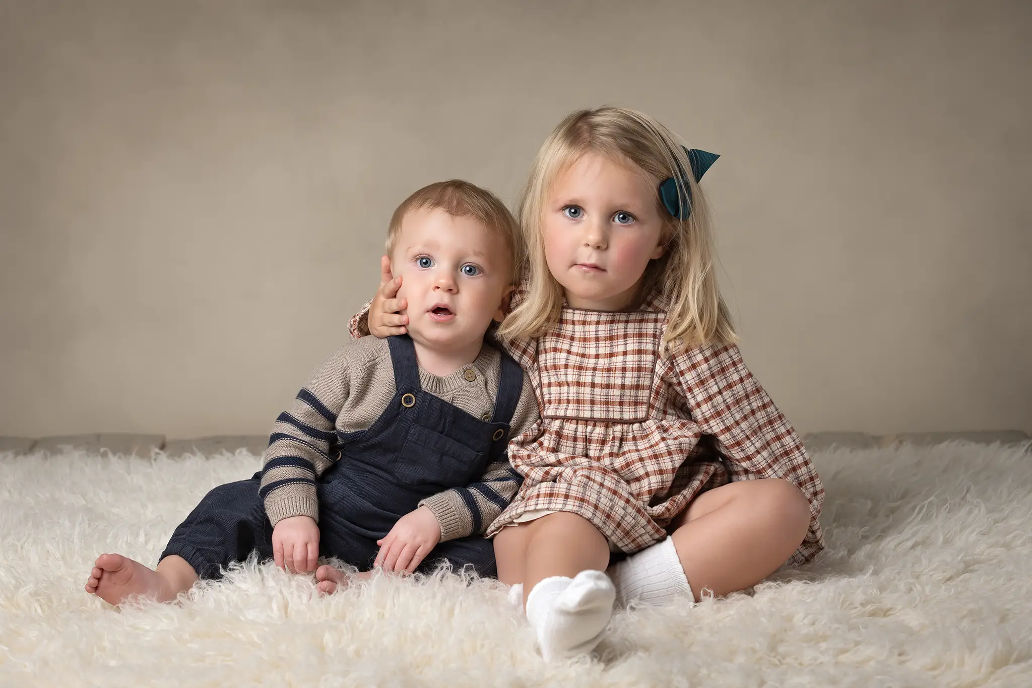Syskonfotografering i studio Två syskon sitter på en ljus matta och tittar mot kameran i studioljus.