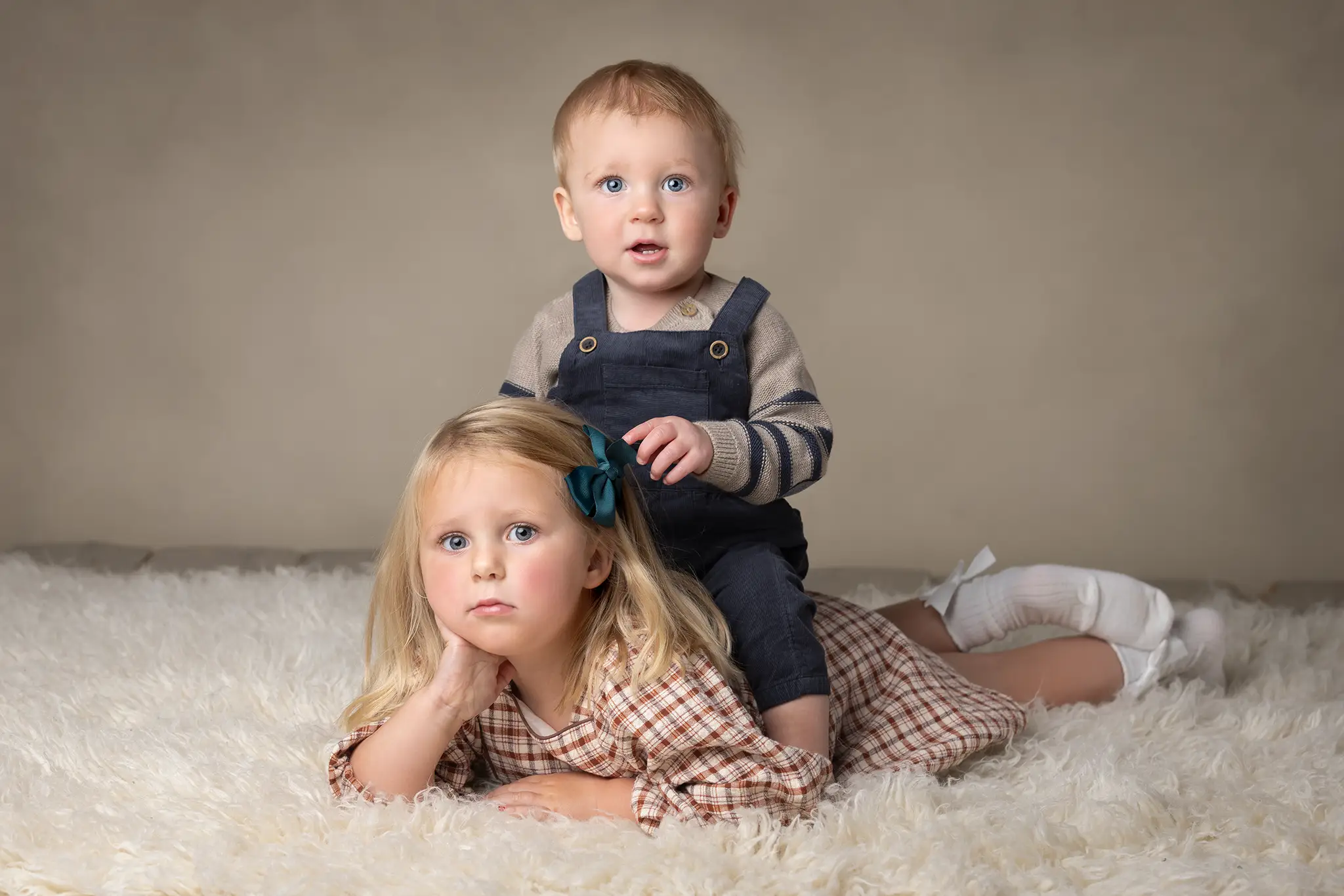 Syskonfotografering i studio Två syskon sitter på en ljus matta och tittar mot kameran i studioljus.