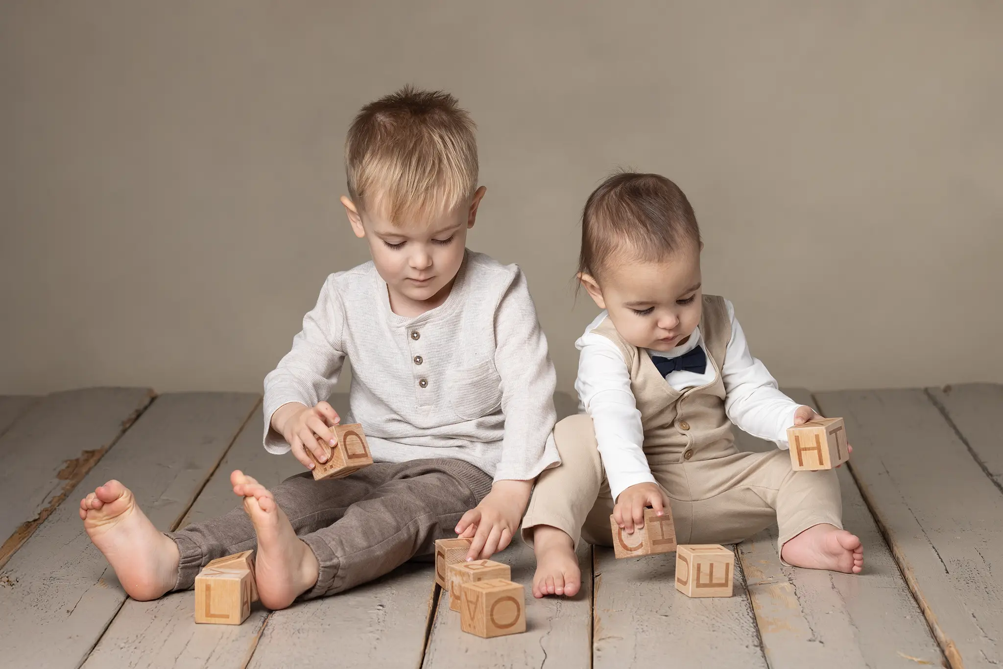 syskonfotografering-lund-barn-leker-med-traklossar Två syskon sitter på studiogolv och leker med träklossar med bokstäver mot neutral bakgrund.