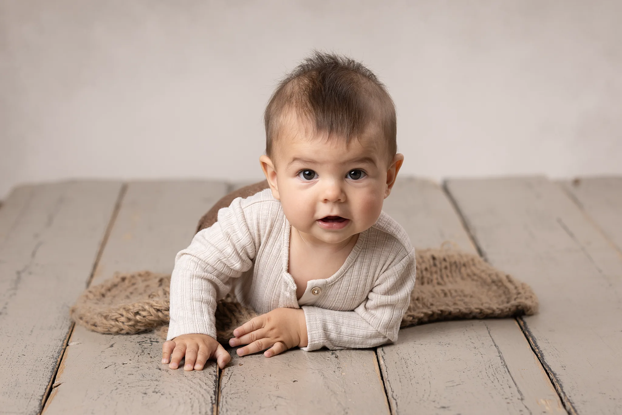 baby-kryper-rustikt-tragolv-studio Baby kryper på rustikt trägolv i neutral studiobelysning och tittar mot kameran.