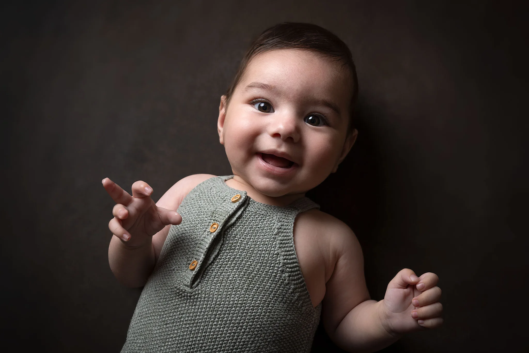 4-månaders baby ligger på brun bakgrund och skrattar mot kameran.