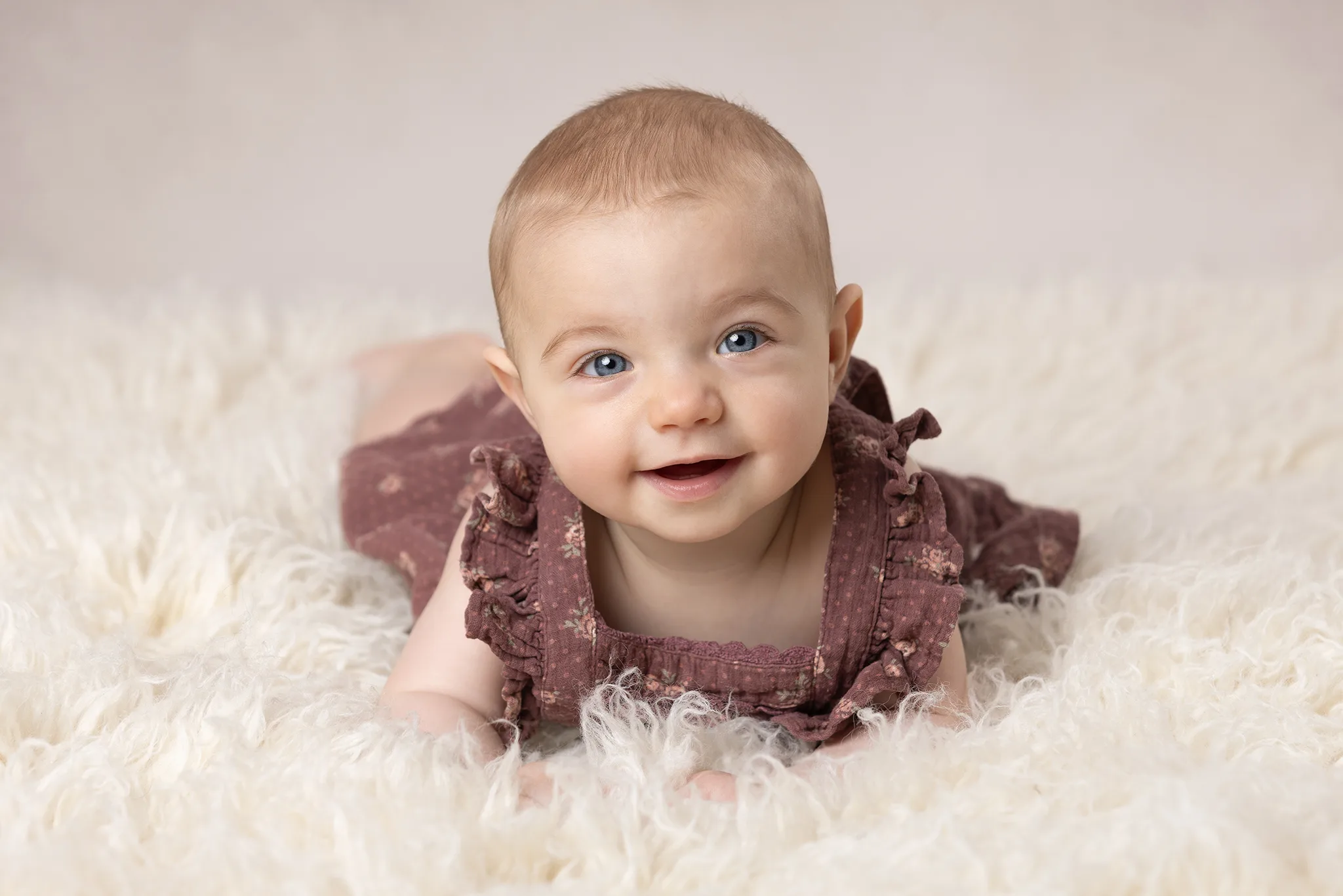 Babyfotografering 6 månader i studio i Lund – bebis på mage på mjuk filt och ler mot kameran