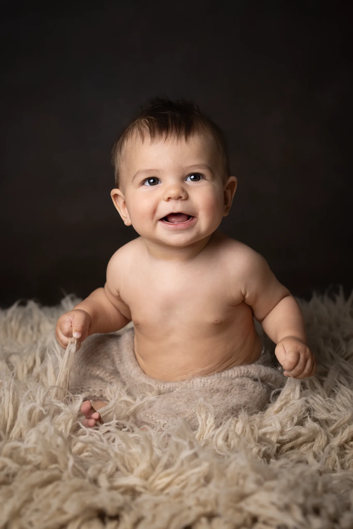 babyfotografering-brun-bakgrund-med-fall-glad-bebis-studio-lund Glad bebis sitter på mjuk fäll mot brun bakgrund i studio