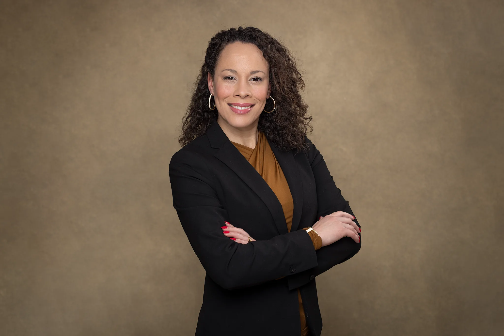 Professionellt porträtt: person i svart kavaj med armarna i kors mot beige studiobakgrund.