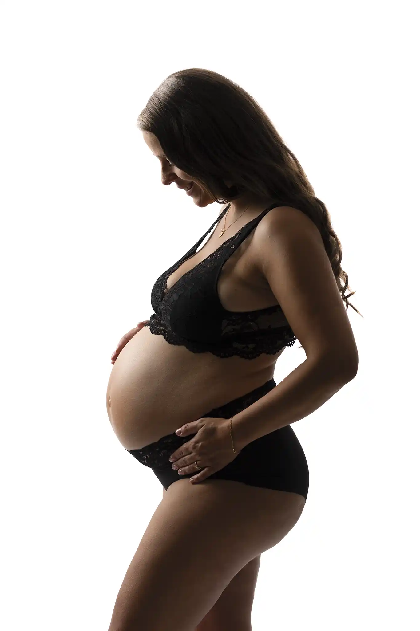 Gravid kvinna med svarta underkläder som poserar på vit bakgrund.