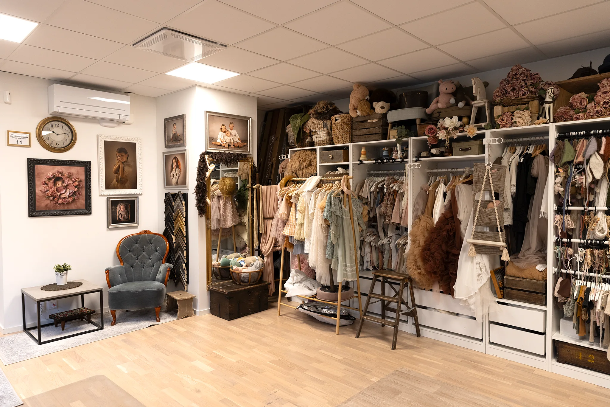 Studiointeriör med rekvisitagarderob för babyfotografering: klänningar, wraps och accessoarer på rad.