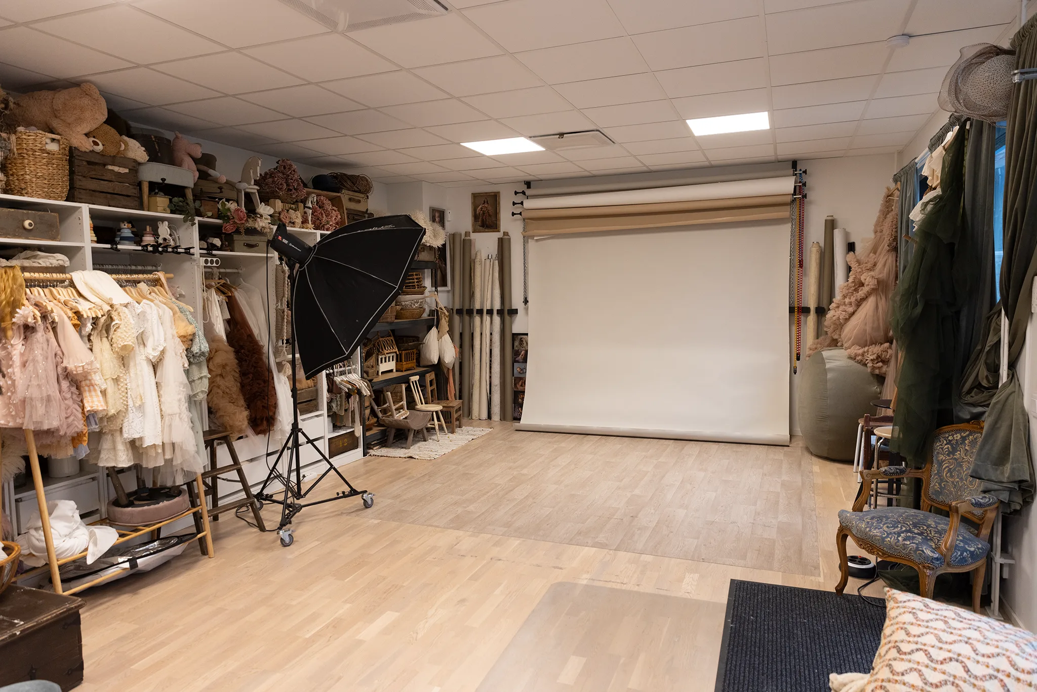 Studioyta med vit fotobakgrund, blixt med softbox och rekvisita för babyfoto på hyllor.