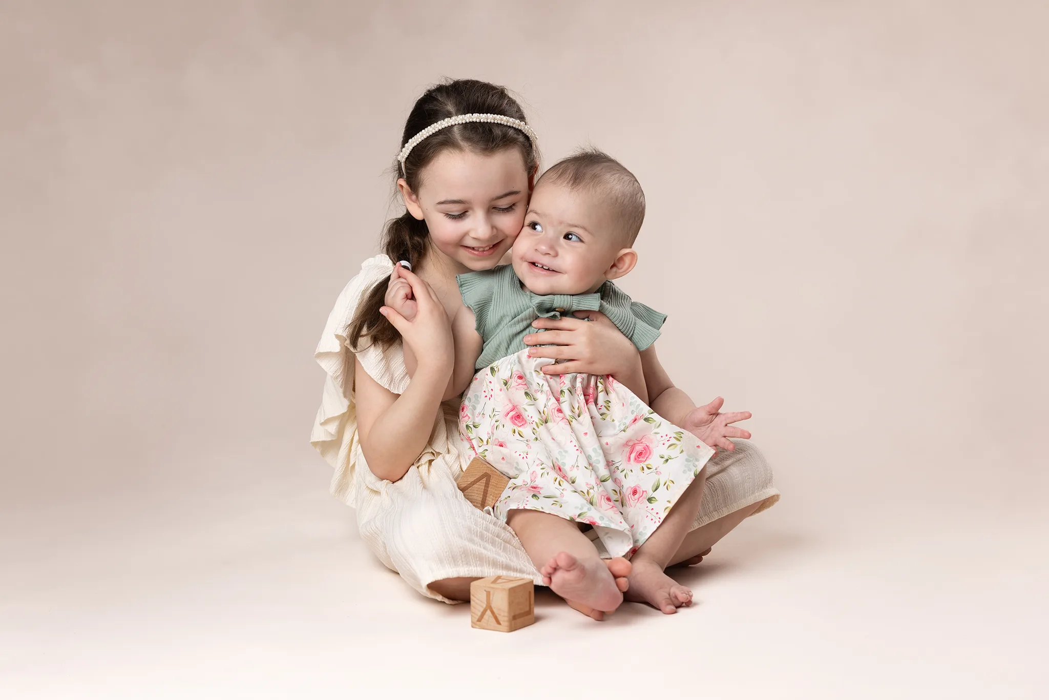 Syskon sitter och kramar på beige bakgrund.