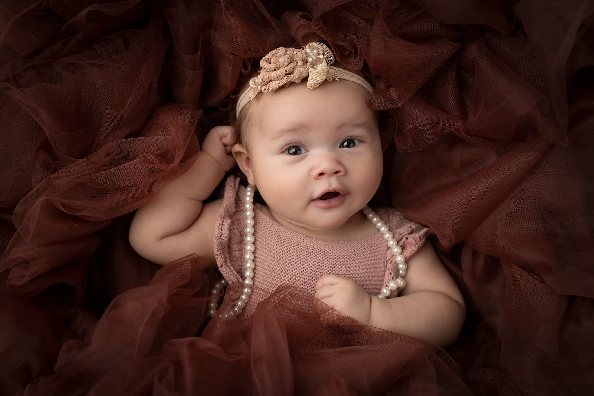 babyfotografering-lund-kreativt-babyportratt-tyll Baby ligger i vinröd tyll och har pärlhalsband, fotograferad i studio.