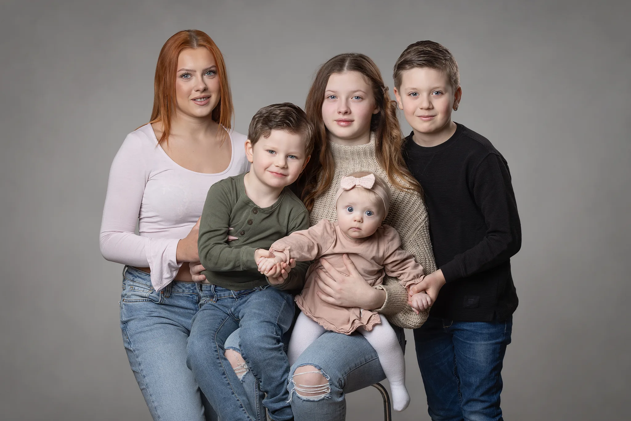 familjefotografering-lund-syskonportratt-studio Syskonporträtt i studio med fyra barn och en baby mot grå bakgrund.