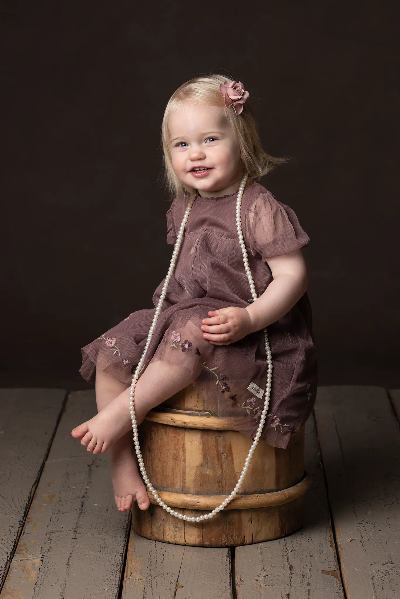 En liten flicka sitter på en pall med ett pärlhalsband.