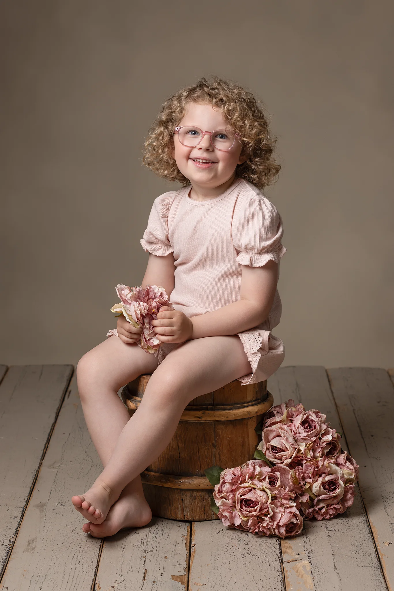 barnfotografering-lund-flicka-pa-trabalja-med-rosa-blommor Barnfotografering i Lund av liten flicka med lockigt hår sittande på en träbalja omgiven av rosa blommor.