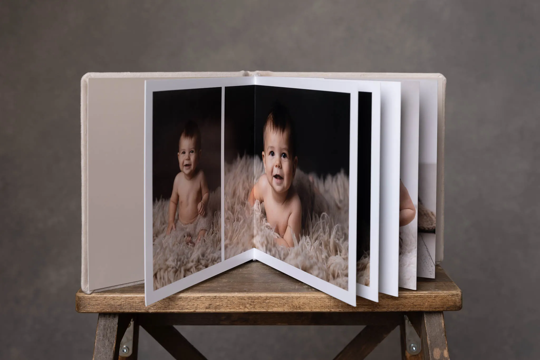 Öppet fotoalbum med tjocka uppslag och bilder från en babyfotografering