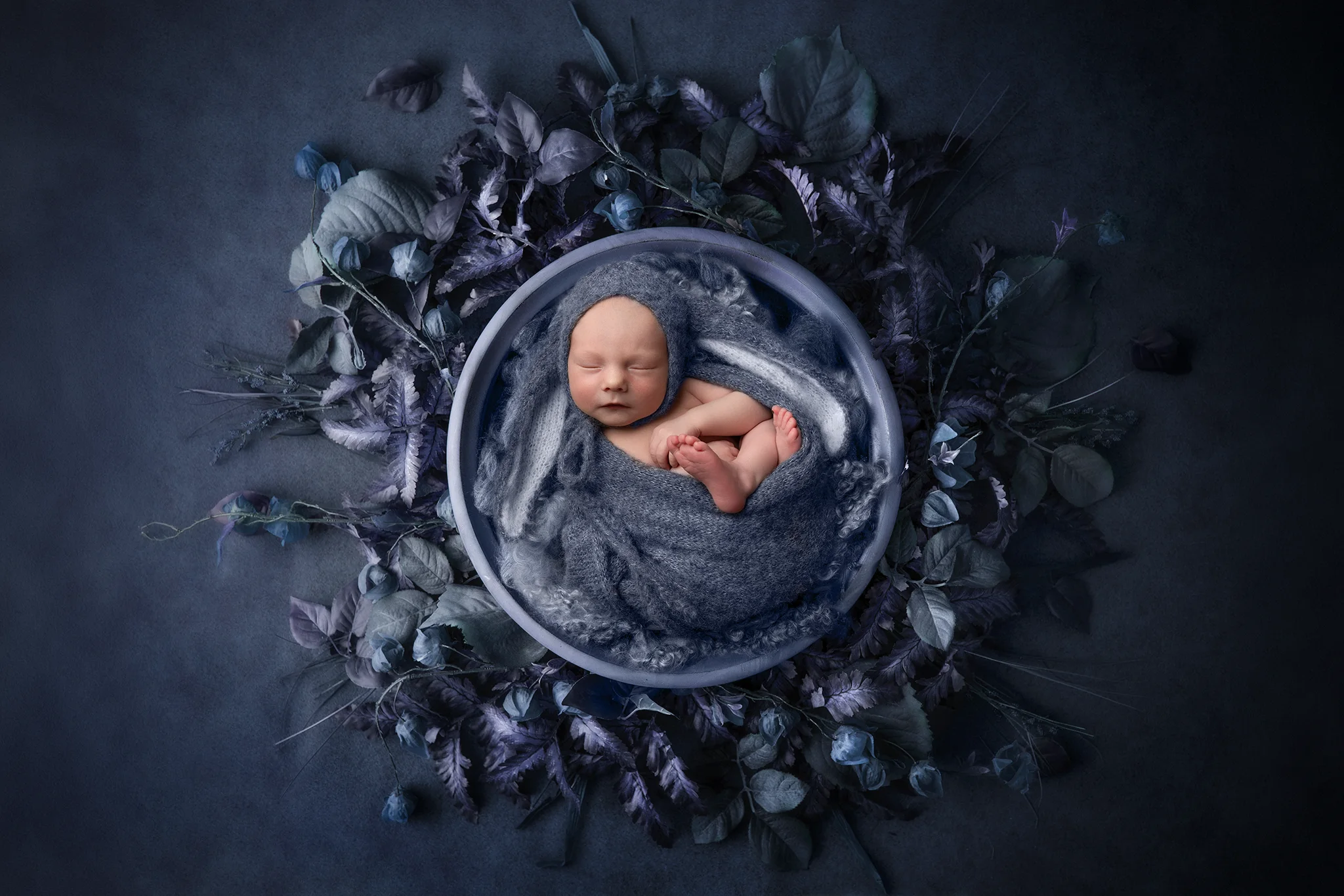 nyfoddfotograf-lund-bla-nyfoddbild Sovande nyfödd bebis omgiven av blå blommor under nyföddfotografering i Lund